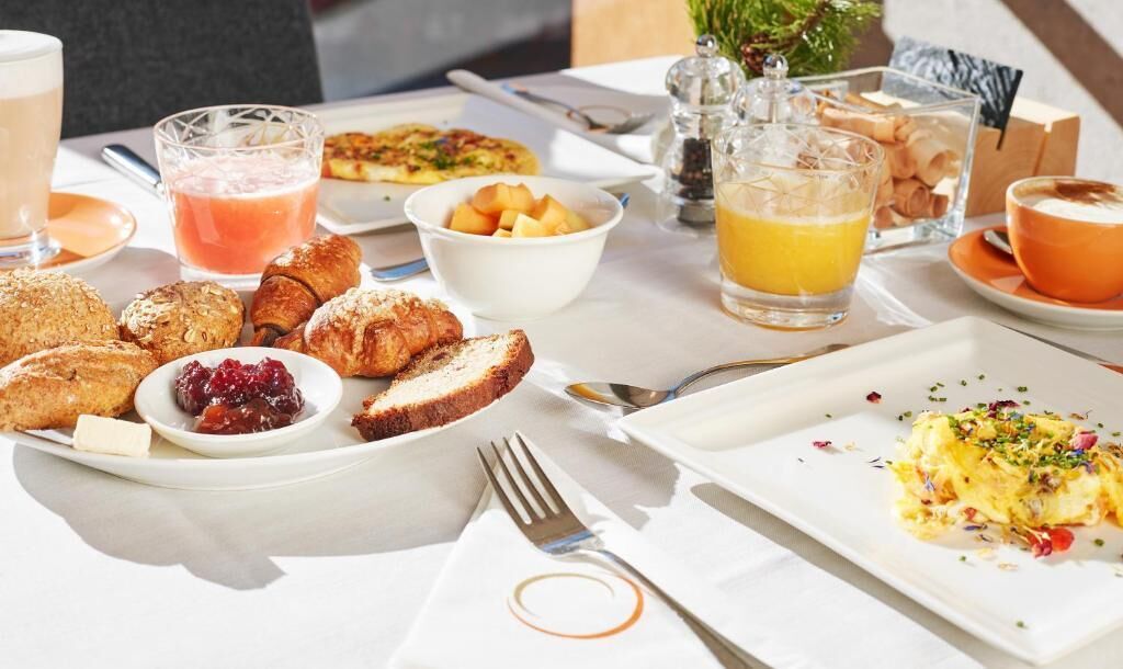 Una mesa con croissants, tostadas, fruta y huevos revueltos para el desayuno.