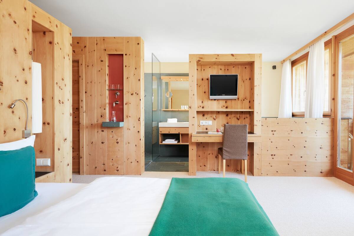 A wooden room with a bed, a desk, a chair, a TV, and a bathroom.