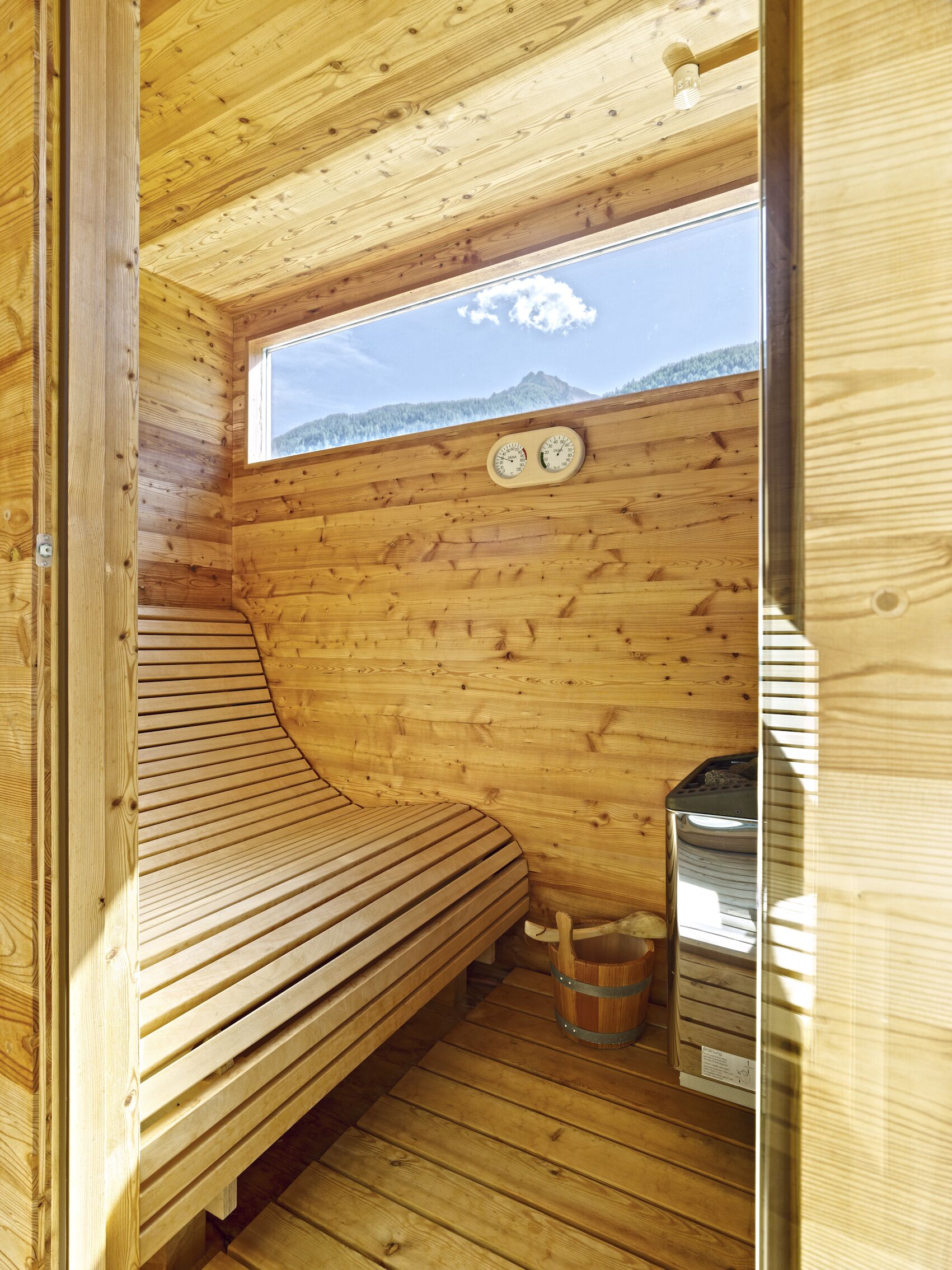 A wooden cabin room with a bench, a window with a view of mountains, and a sauna.