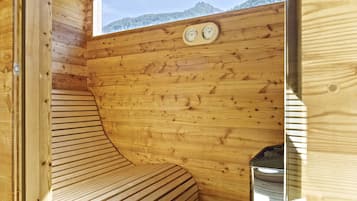 A wooden cabin room with a bench, a window with a view of mountains, and a sauna.