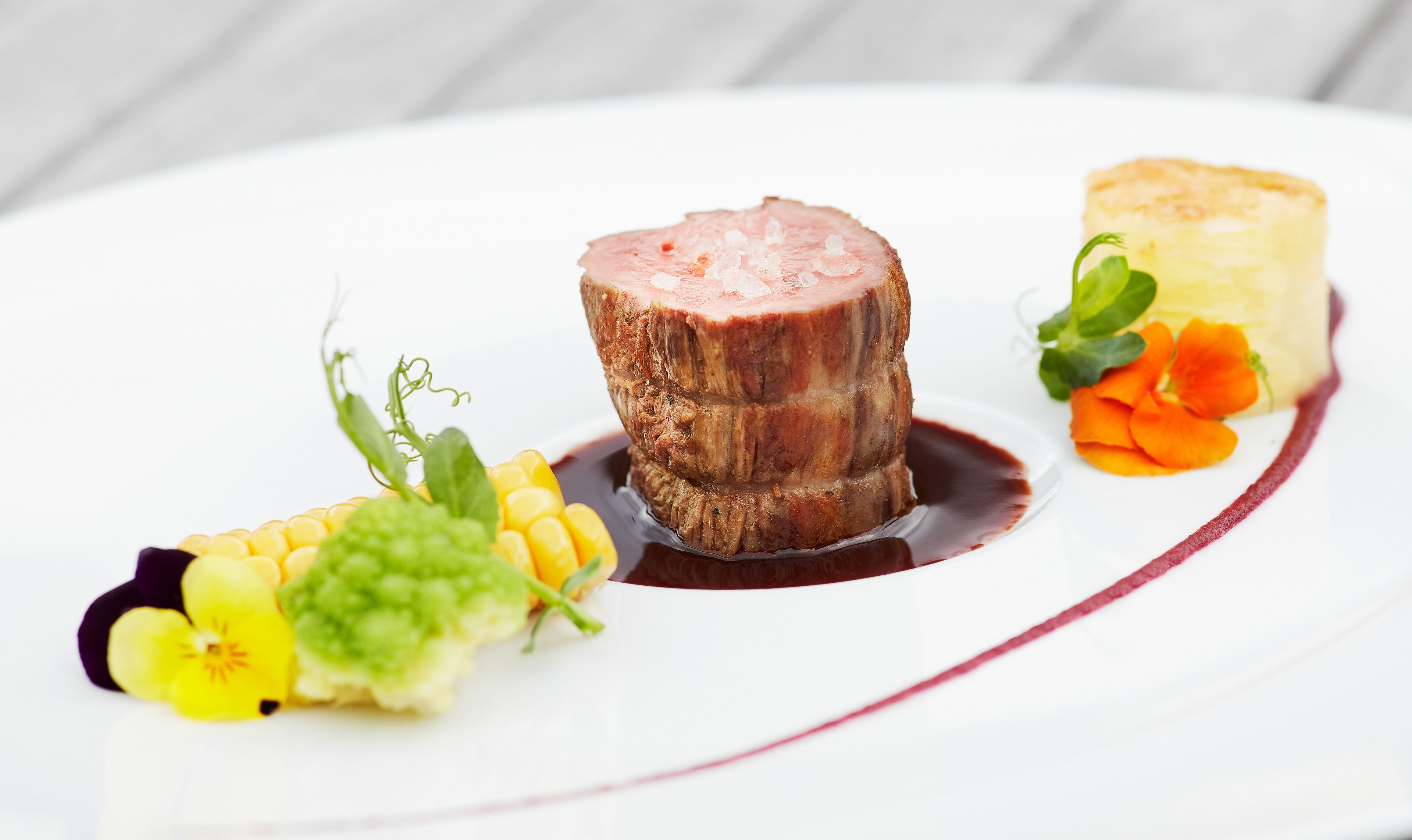 A plate with a piece of meat, a pastry, and some vegetables.