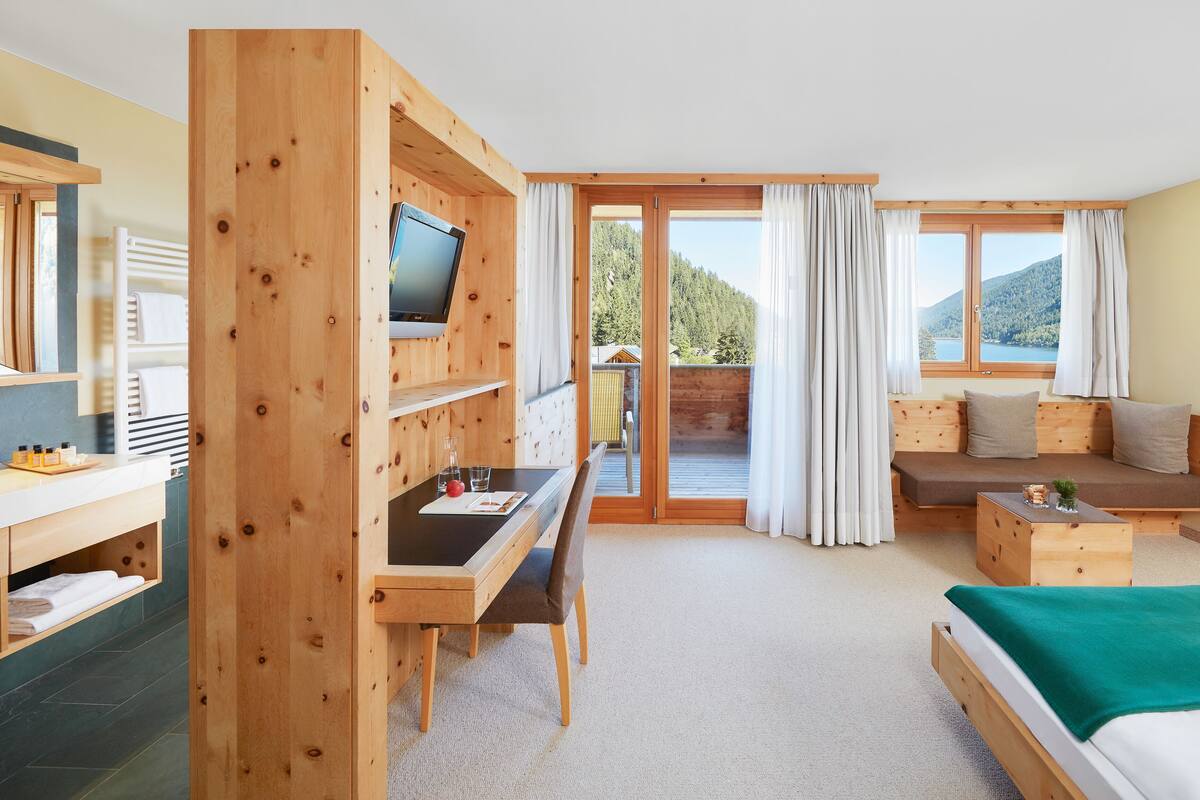 A modern room with a wooden desk, a bed, a sofa, and a TV.