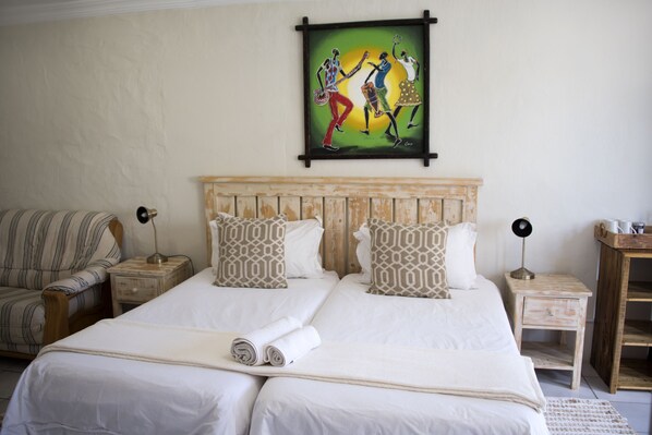 A double bed with white linens, two nightstands with lamps, a striped armchair, and a wall painting.