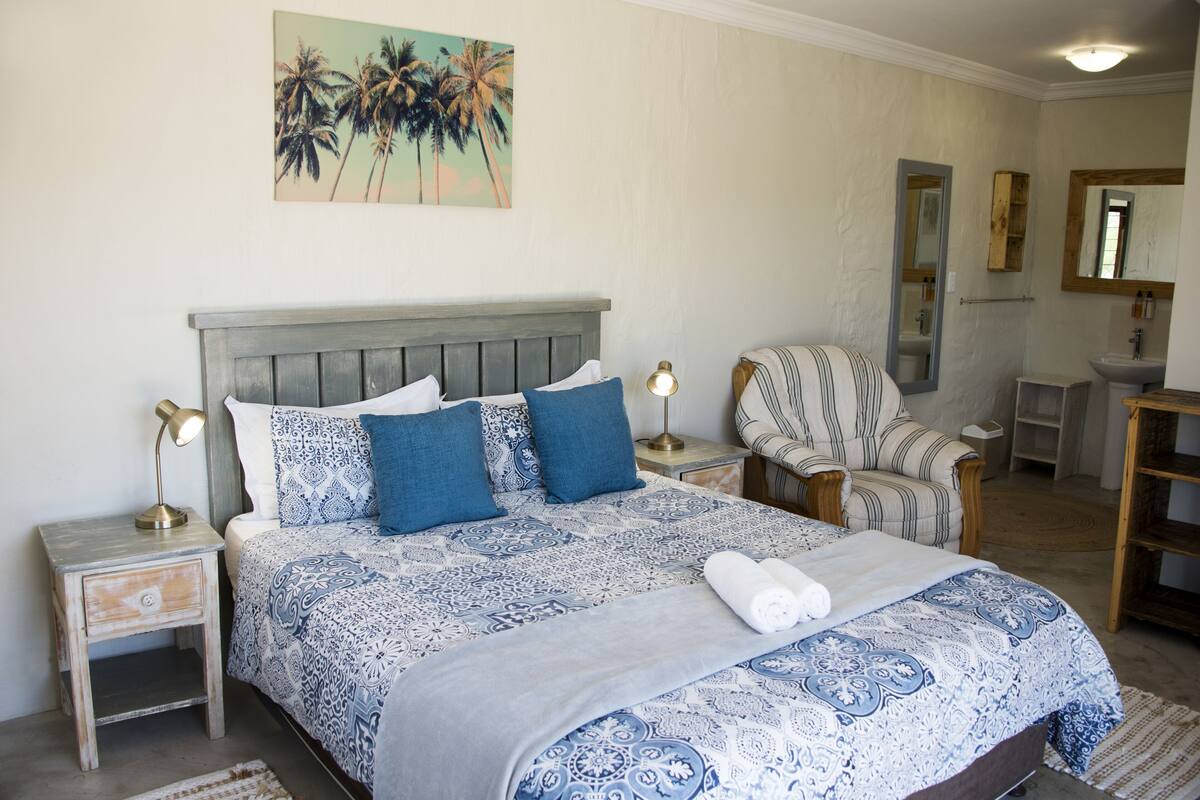 A bedroom with a bed, nightstands, a chair, a mirror, and a painting on the wall.