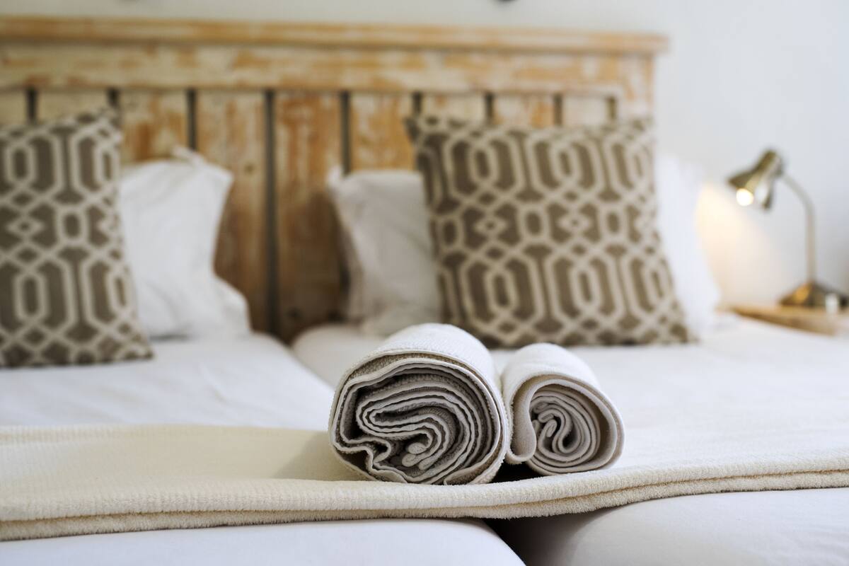 A neatly made bed with rolled towels, patterned pillows, and a bedside lamp.