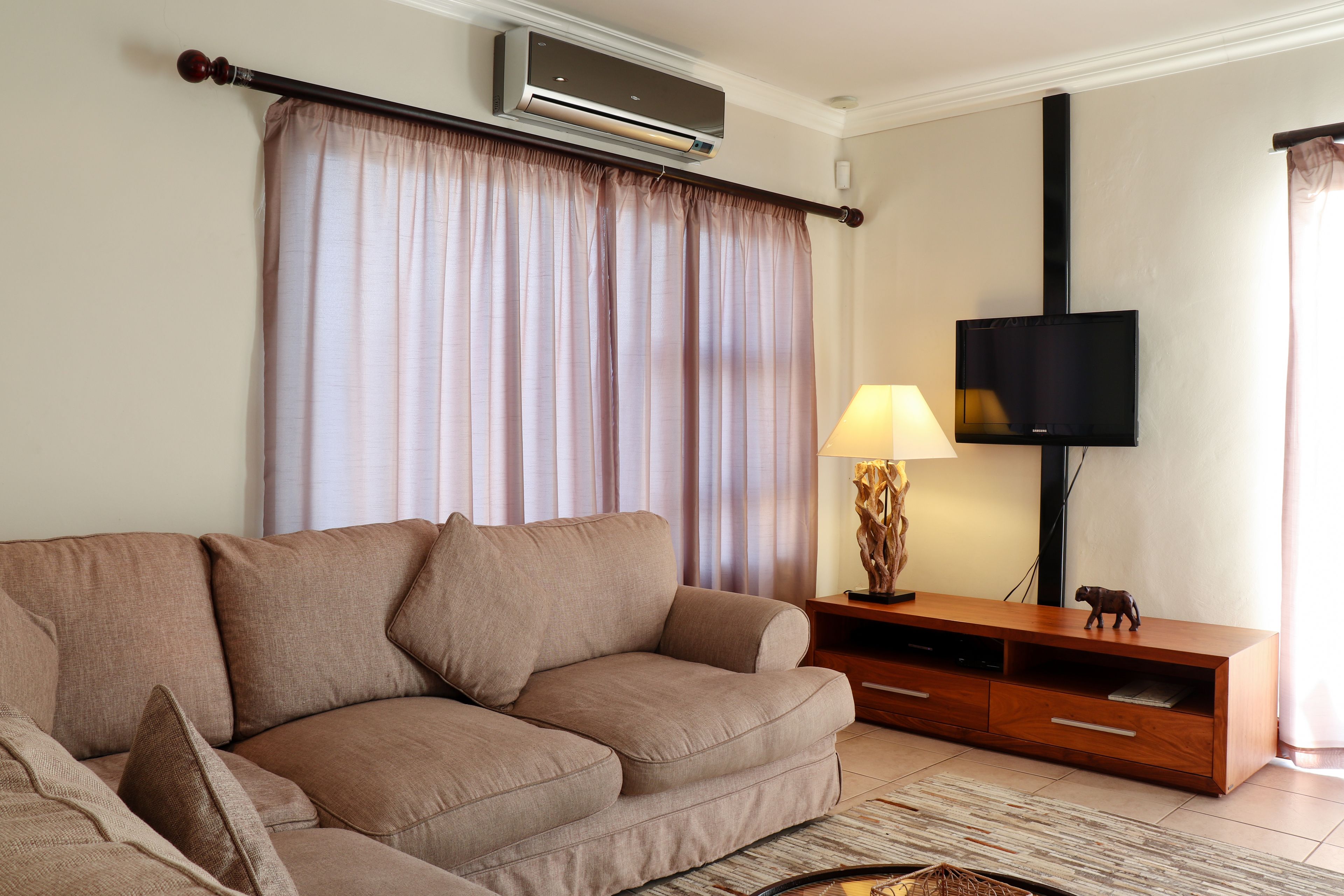 Una sala de estar con un sofá color beige, un mueble de madera para el entretenimiento, un televisor de pantalla plana y una lámpara.