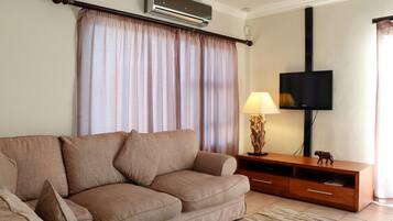Una sala de estar con un sofá color beige, un mueble de madera para el entretenimiento, un televisor de pantalla plana y una lámpara.