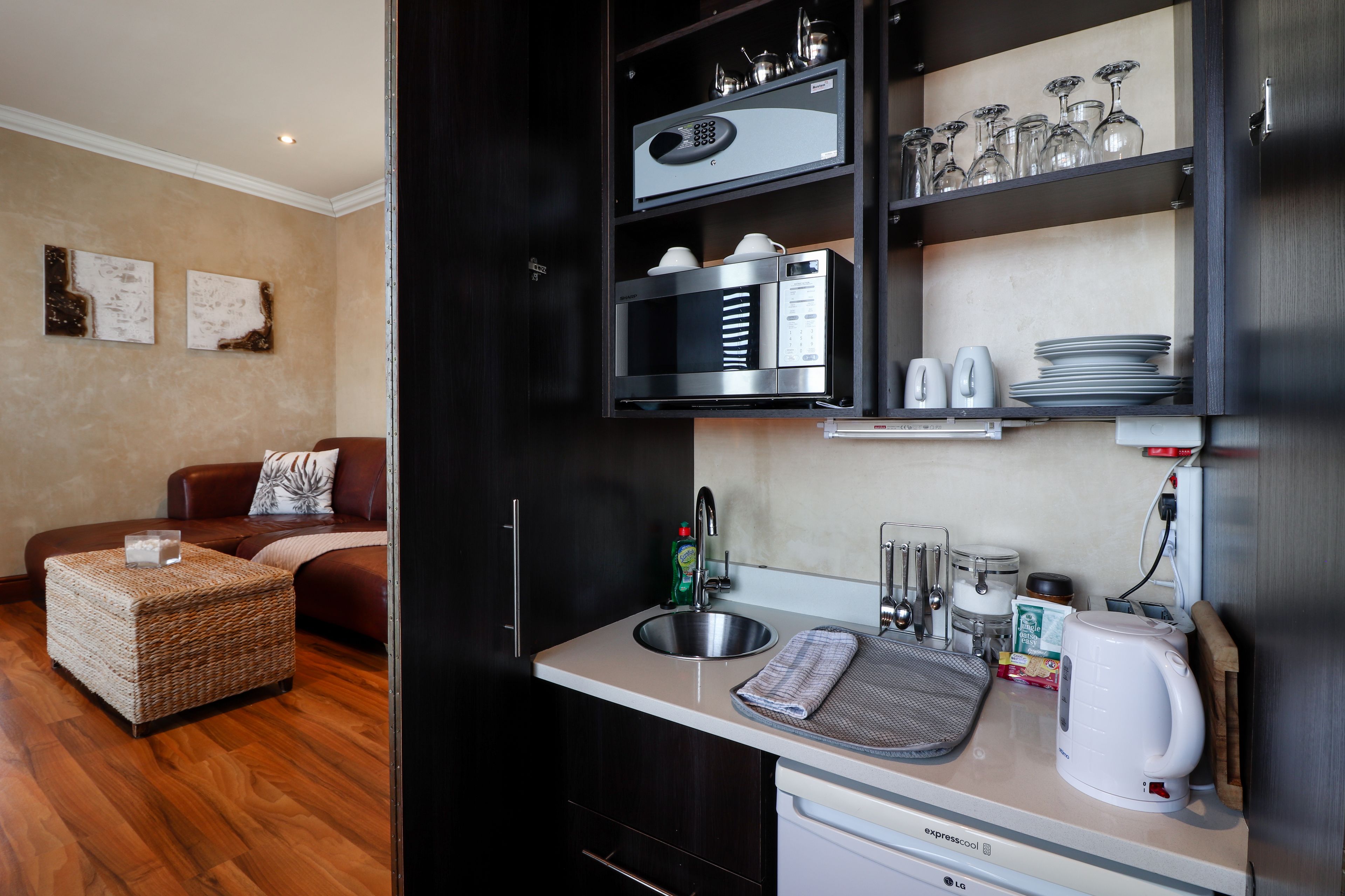 Cocina compacta con microondas integrado, cafetera y hervidor. Cuenta con un comedor con sofá y una mesa pequeña.