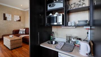 Cocina compacta con microondas integrado, cafetera y hervidor. Cuenta con un comedor con sofá y una mesa pequeña.