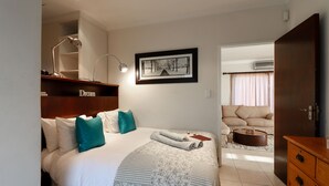 Een slaapkamer met een bed, een bureau, een stoel, een ingelijst schilderij en een kledingkast.