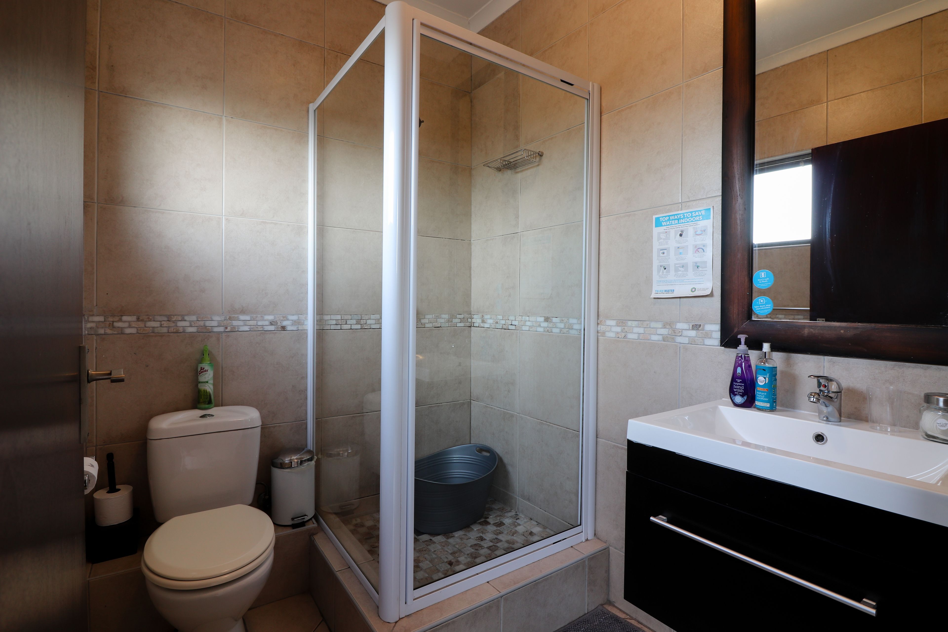 A bathroom with a toilet, a shower enclosure, a sink, and a mirror.