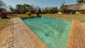 A rectangular swimming pool with clear blue water, surrounded by a brick border and a stone edge. - Blue Cottages (Hoedspruit)