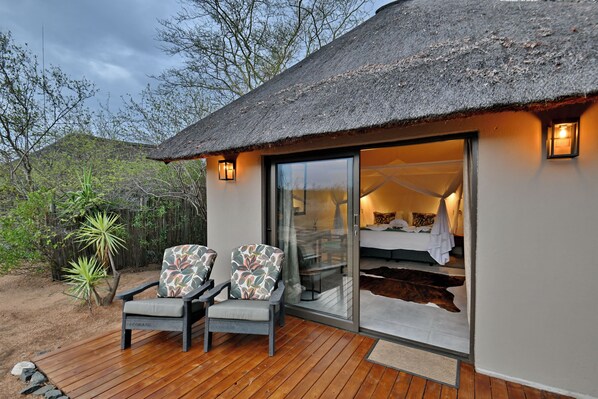 A thatched-roof structure with a sliding glass door leading to a bedroom with a bed and a nightstand. - Masodini Private Game Lodge (Hoedspruit)
