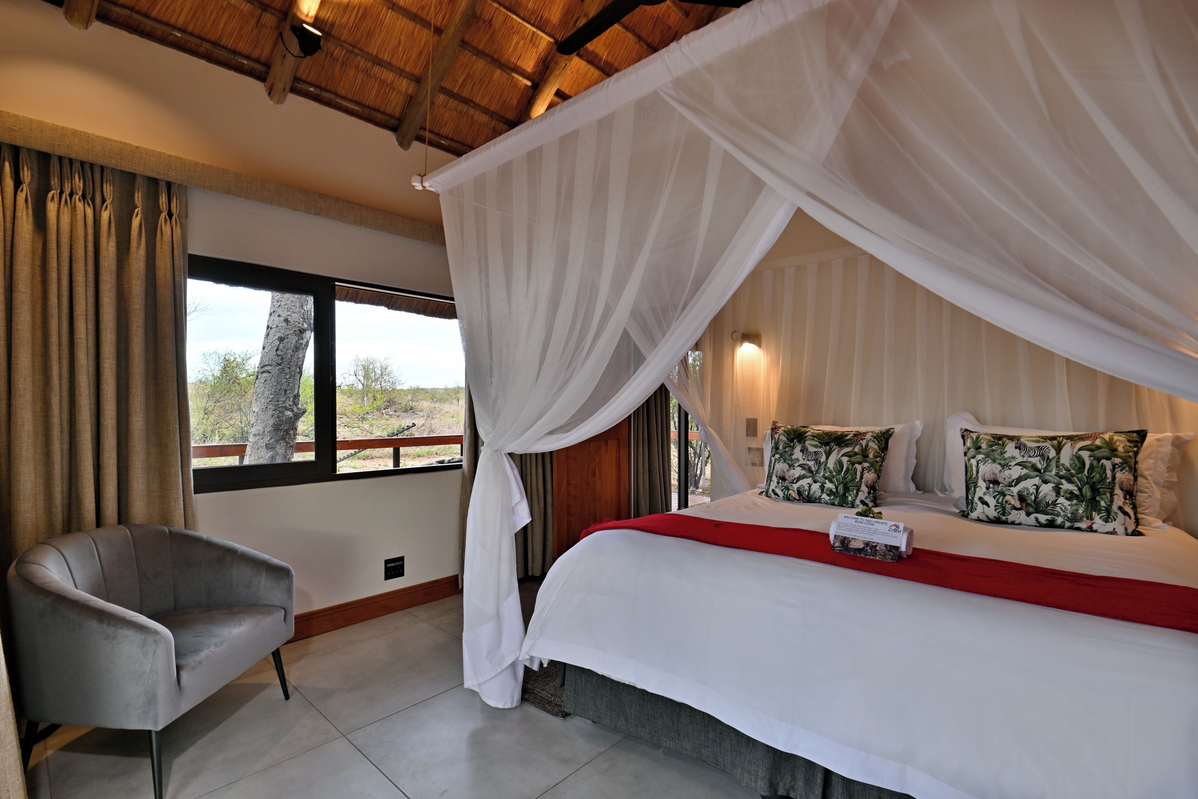 A room with a bed, a chair, a window with curtains, and a view of the outdoors.