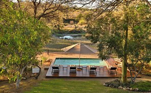 A swimming pool with a deck and lounge chairs, surrounded by trees and a natural landscape. - Masodini Private Game Lodge (Hoedspruit)