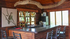 A rustic bar area with a wooden bar counter, multiple stools, and a large window providing natural light.
