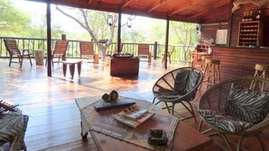 A wooden deck with outdoor seating, including chairs and a table, surrounded by a wooden fence and trees.
