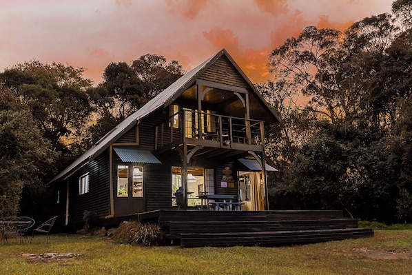 A wooden cabin with a balcony, a porch, and a dining area.