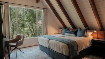 A bedroom with a large window, a bed with pillows, a chair, and a bedside table.