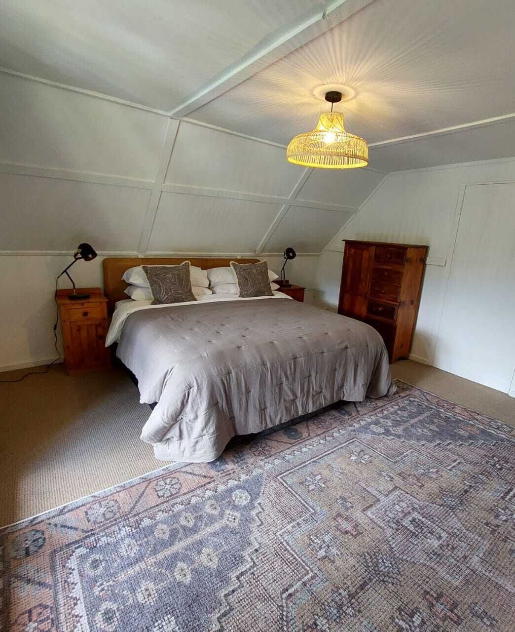 Un dormitorio con una cama grande, un tapete estampado, un armario de madera y una lámpara colgante.