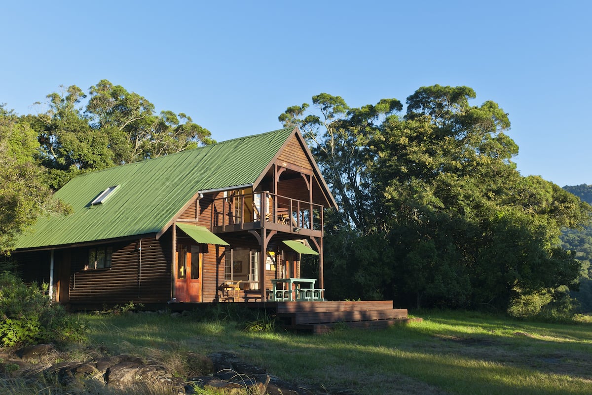 A wooden cabin with a green roof, a balcony, and a porch with outdoor seating.