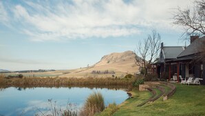 A serene lakeside setting with a house featuring a patio with outdoor furniture. - Rockwood Lodges (Karkloof Nature Reserve)