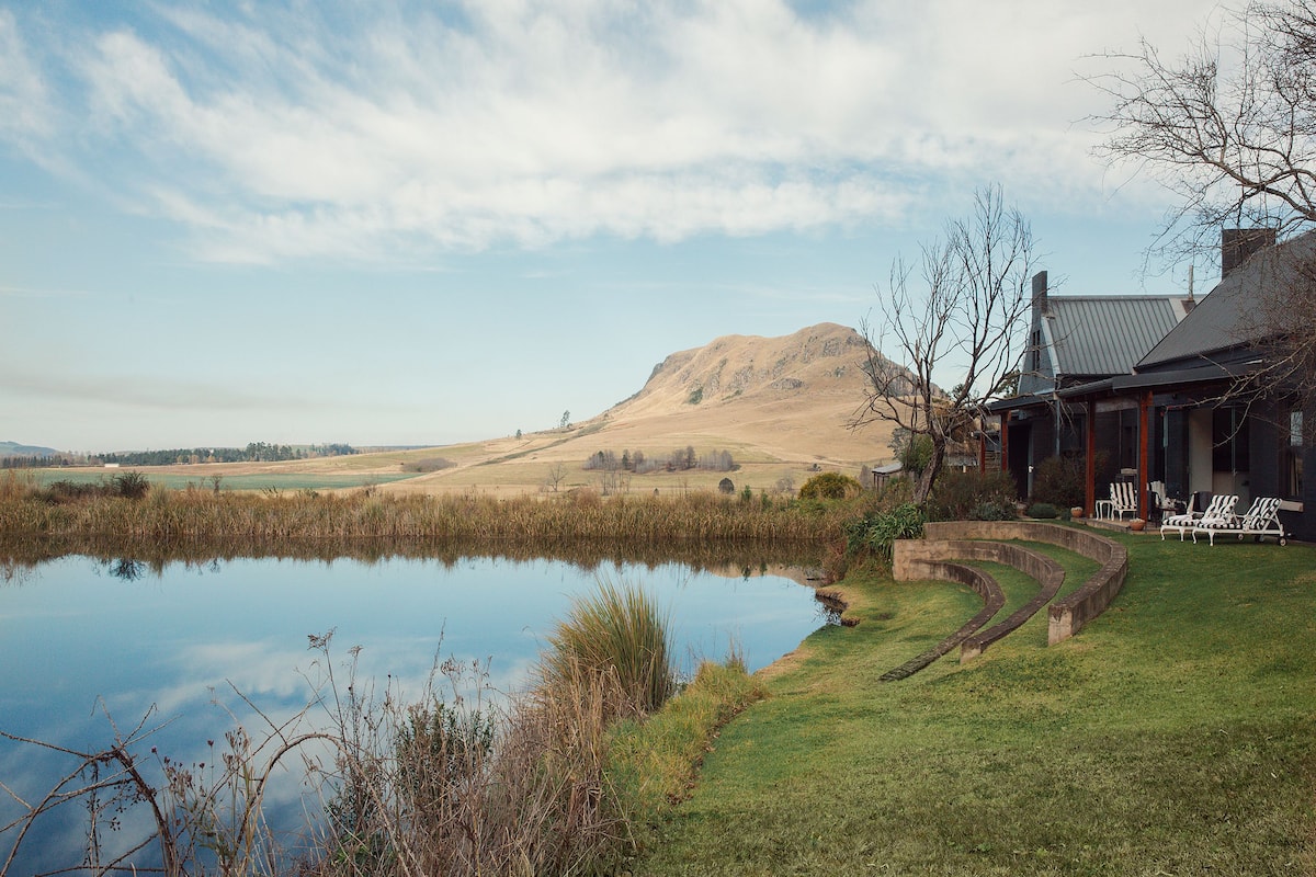 A serene lakeside setting with a house featuring a patio with outdoor furniture.