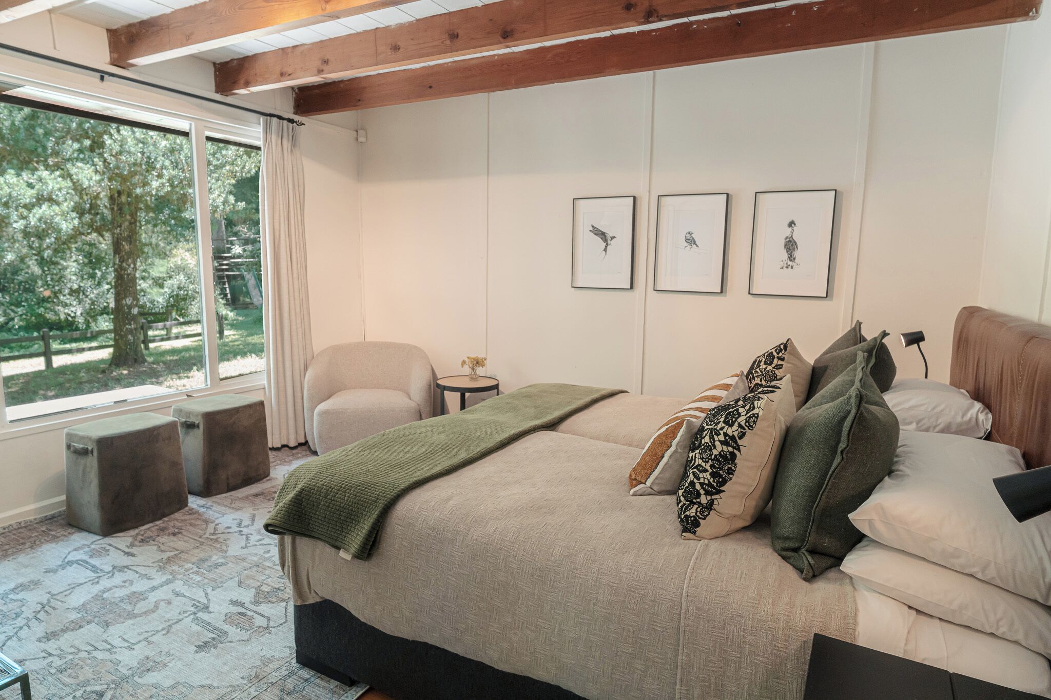 A bedroom with a large bed, a chair, a small table, and framed artwork on the wall.
