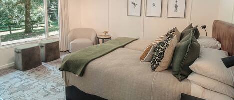 A bedroom with a large bed, a chair, a small table, and framed artwork on the wall.