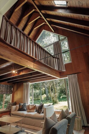 A spacious loft with a high ceiling, a mezzanine level, and large windows offering a view of the outdoors.