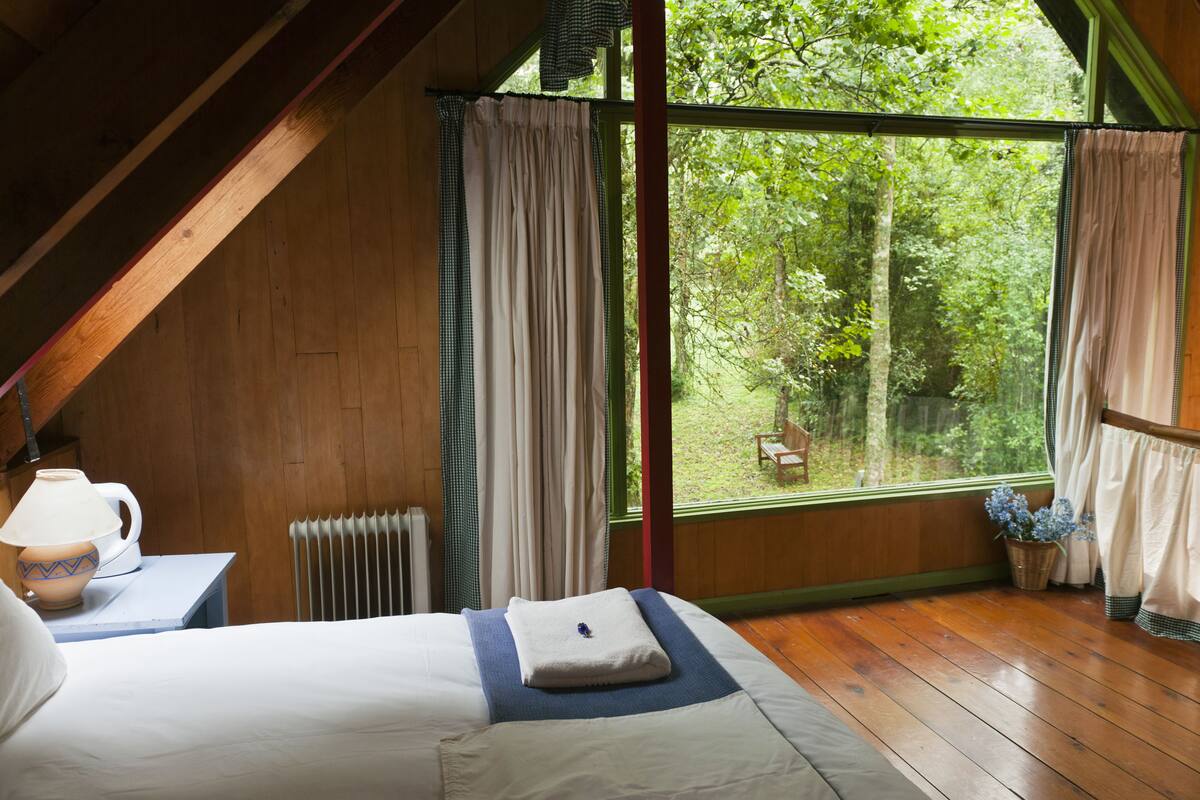 A bedroom with a large window, wooden floor, and a bed with a folded towel.