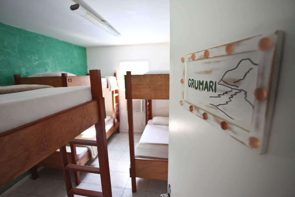 A dormitory room with bunk beds, a green wall, and a sign with 'GRUMARI' and a map.
