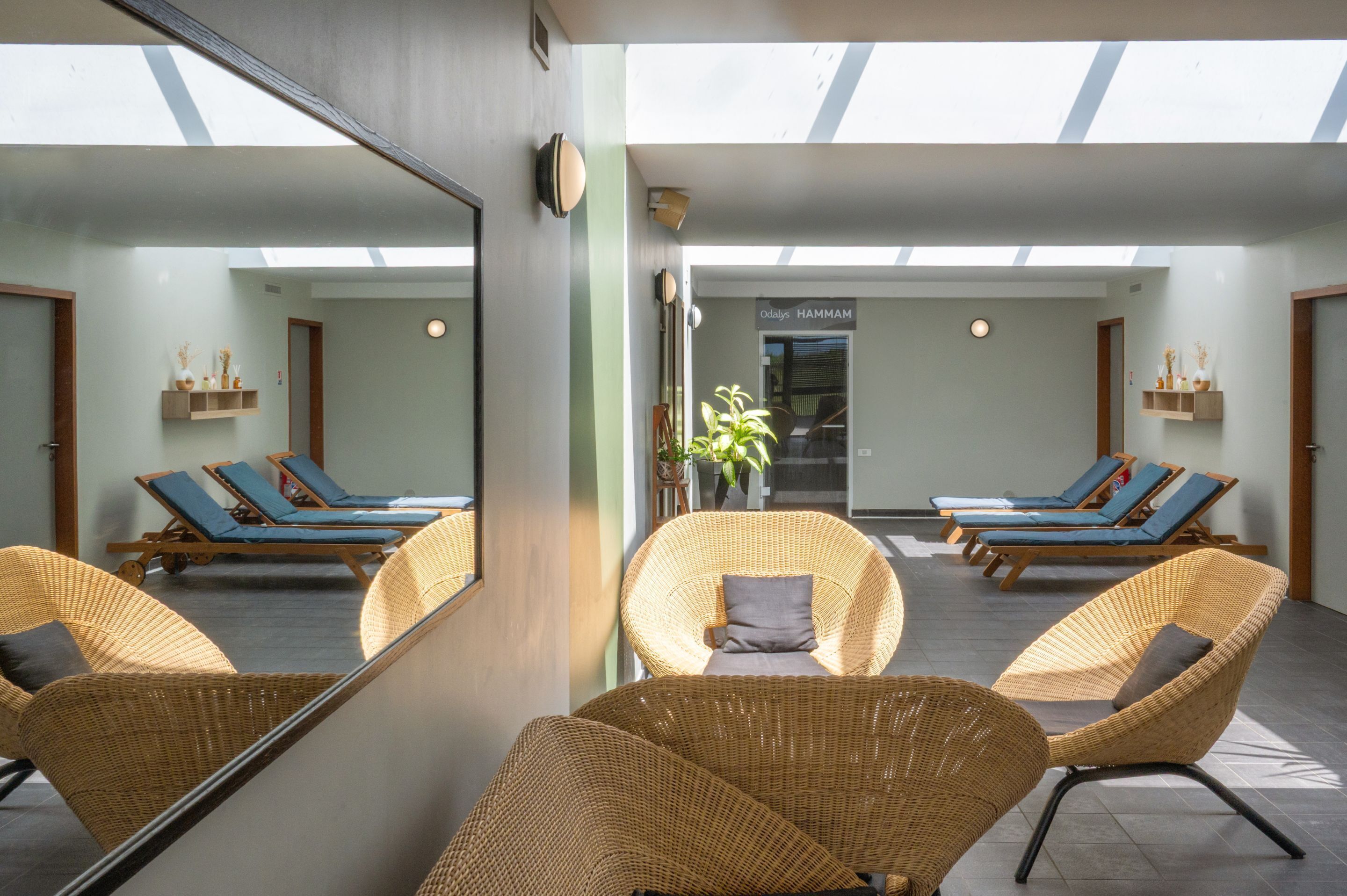 A sunlit room with wicker chairs, a large mirror, and a sign reading "Odalis HAMM."