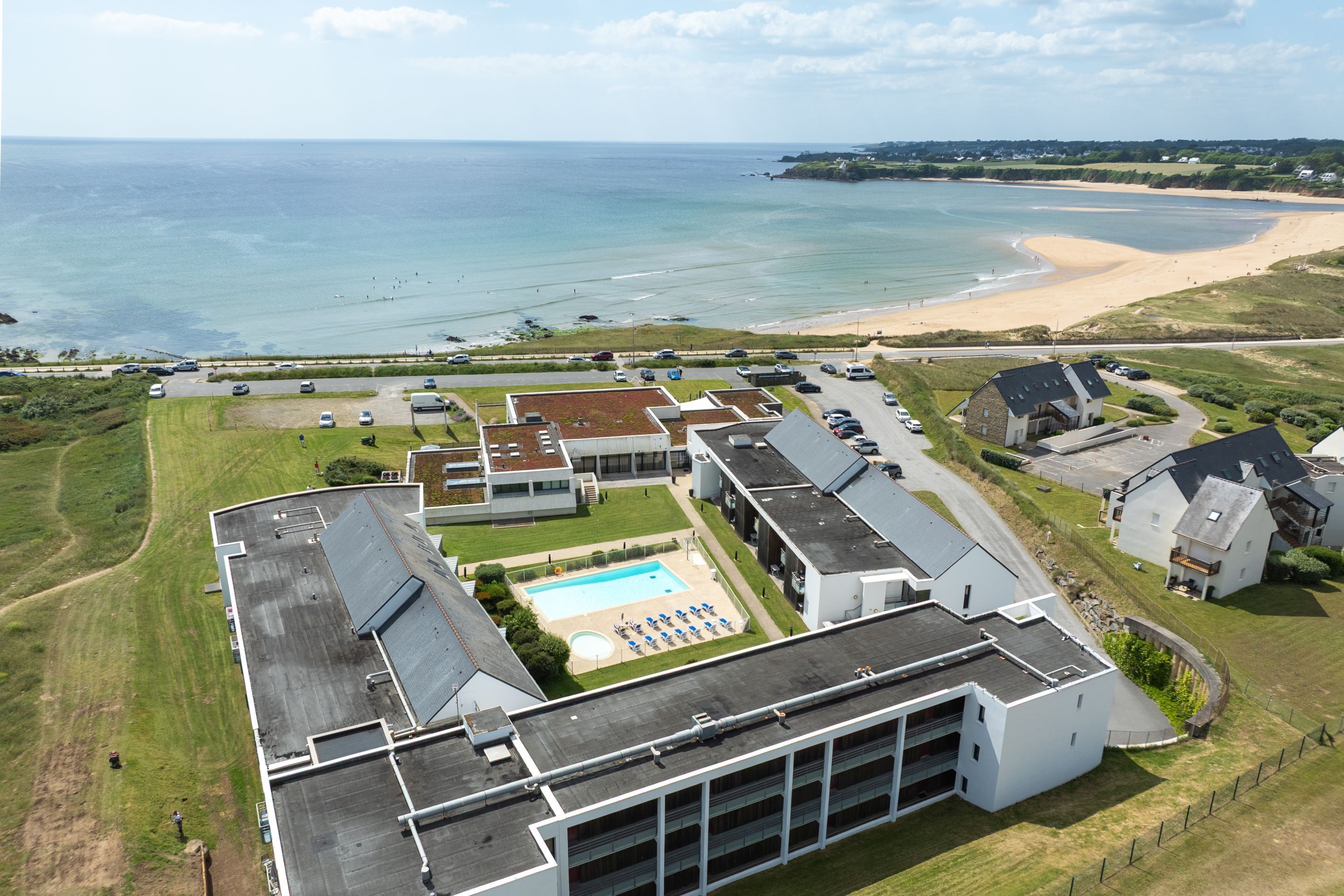 Ein Luftbild eines Küstenhotels mit Schwimmbad, Zugang zum Strand und einem Parkplatz.
