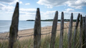 A beach with a wooden fence in the foreground, a sandy shore, and a clear sky with clouds. - Résidence Odalys Fleur de Sel (Guidel)