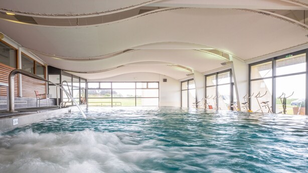 An indoor swimming pool with a view of the outdoors through large windows. - Résidence Odalys Fleur de Sel (Guidel)
