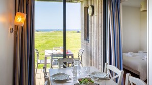 A dining area with a table set for two, a view of the sea, and a bed in the adjacent room. - Résidence Odalys Fleur de Sel (Guidel)