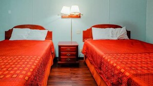 A room with two beds, each with a red bedspread and white pillows, a nightstand with drawers, and a floor lamp between the beds. - Route 66 Inn (Santa Rosa)
