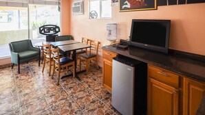 A restaurant with a tiled floor, a table with chairs, a refrigerator, and a television. - Route 66 Inn (Santa Rosa)