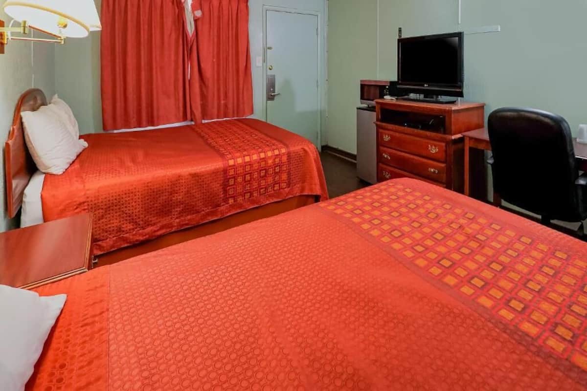 A hotel room with two beds, a television, a desk, and a chair.
