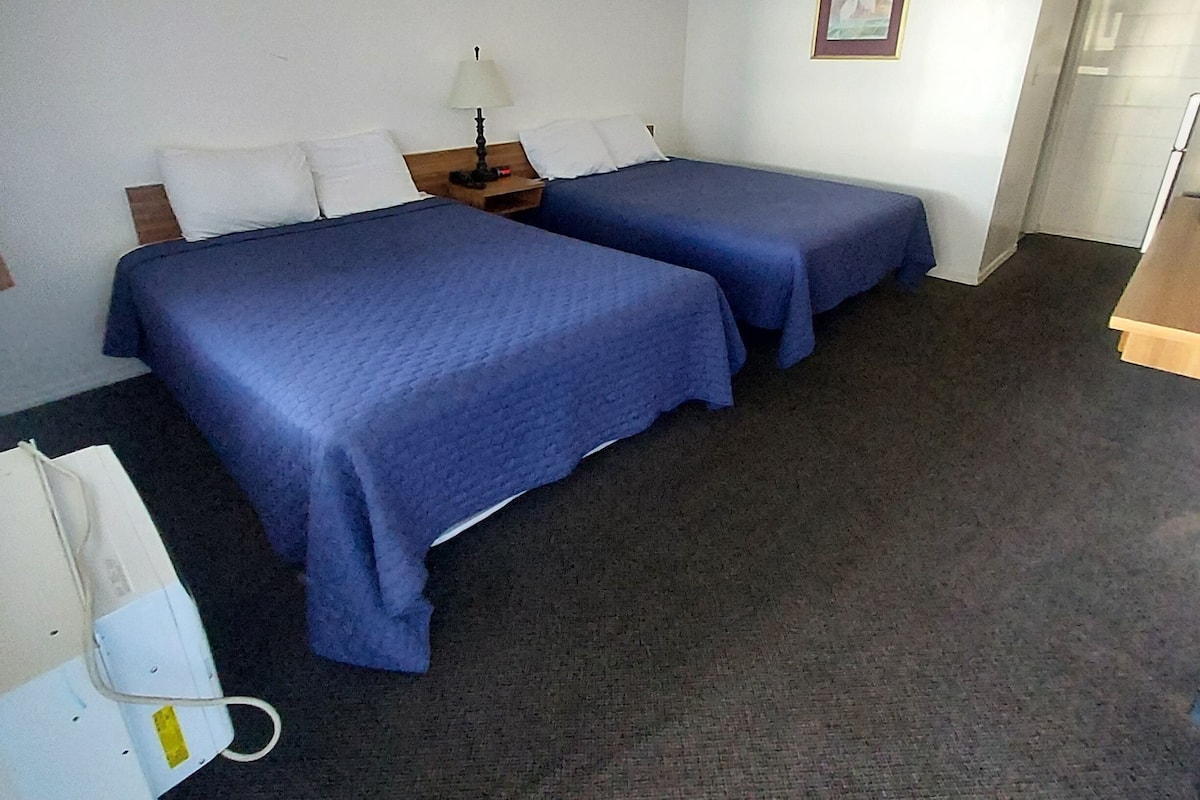 A hotel room with two beds, a desk, a chair, and a telephone.