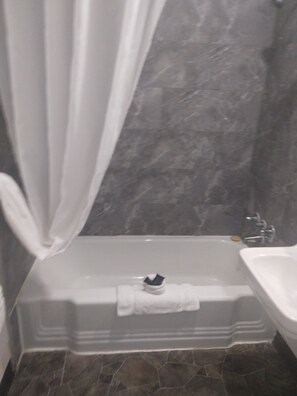 A bathroom with a bathtub, a sink, and a marble wall.