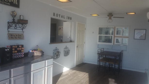 A kitchen with a countertop, cabinets, a dining table with chairs, a ceiling fan, and a window.