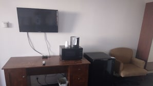 A wooden desk with a flat-screen TV, a coffee maker, and a black speaker.