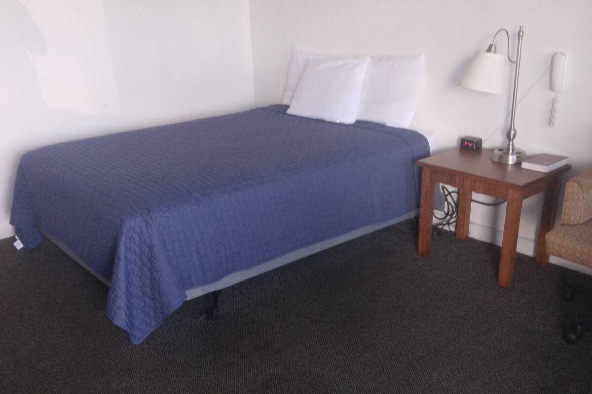 A hotel room with a single bed, a nightstand, a lamp, and a chair.