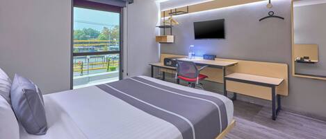 Moderni hotellihuone, jossa on suuri sänky, työpöytä, tuoli, televisio ja näkymä ulos.