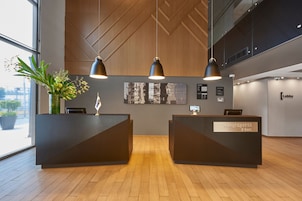A reception area with a modern design, featuring a wooden ceiling, black reception desks, and a large window providing a view outside.