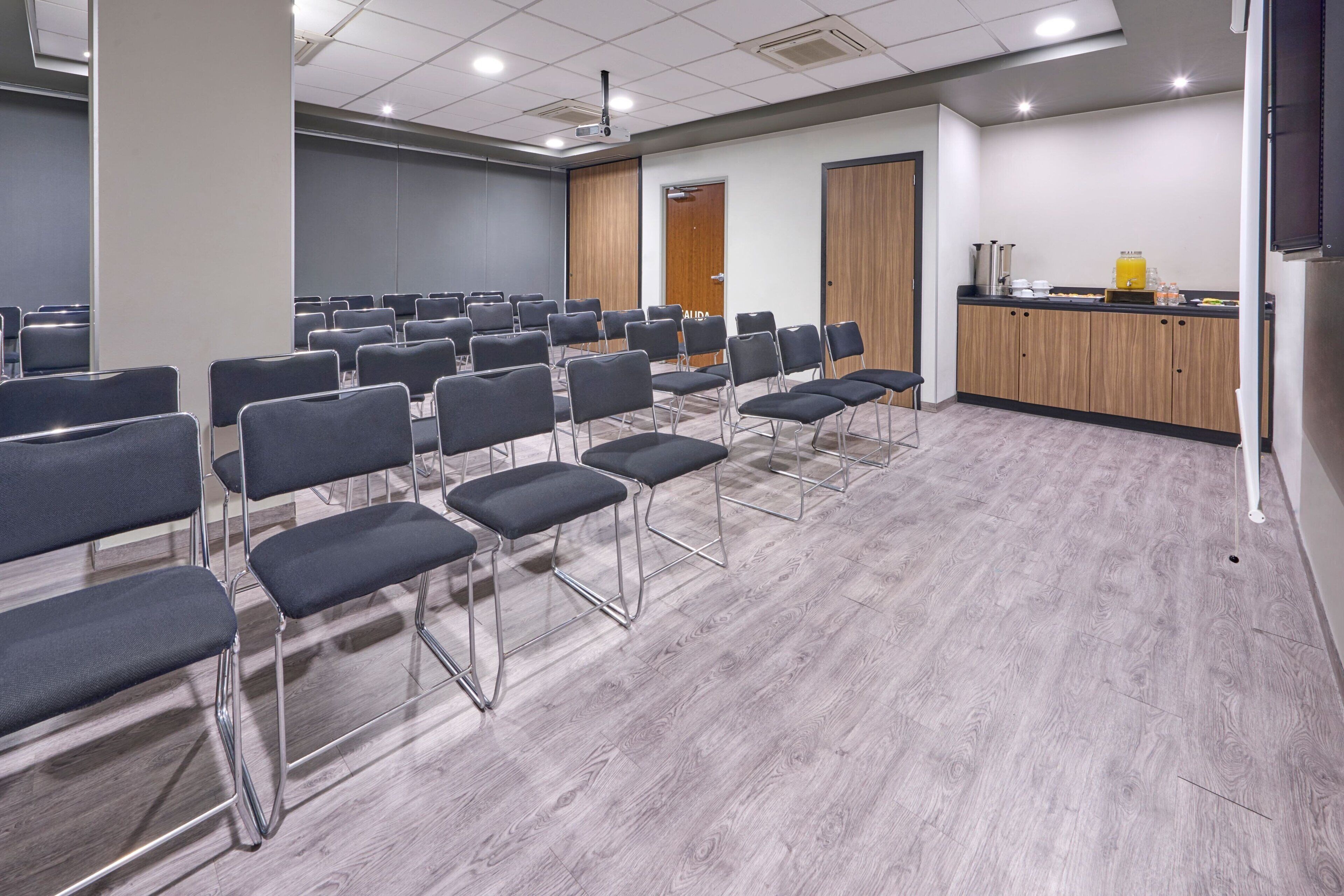 A conference room with rows of chairs, a podium, and a kitchenette area.