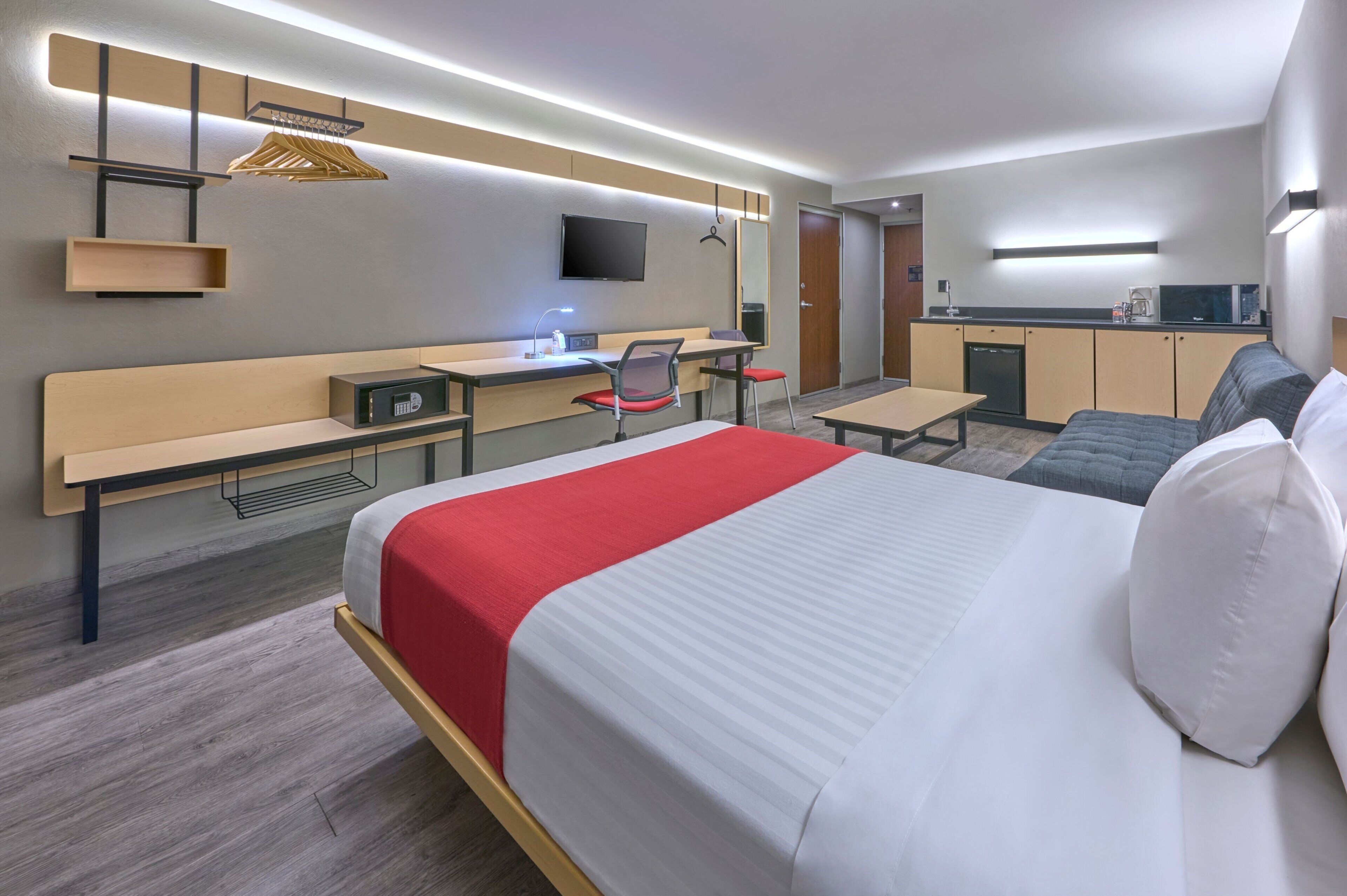 Una habitación de hotel moderna con cama, escritorio, silla y kitchenette.