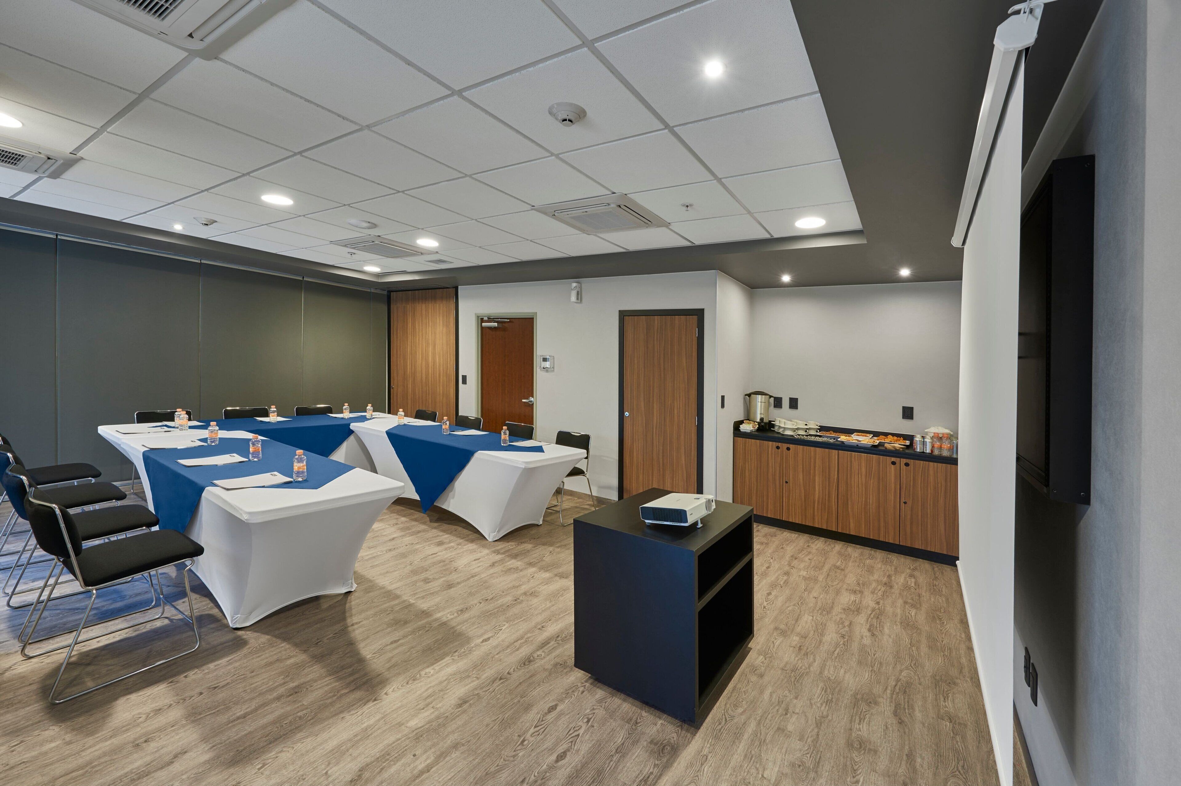 A conference room with tables, chairs, a projector, and a kitchenette.